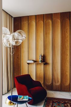 a living room with wood paneling and a red chair in front of a table