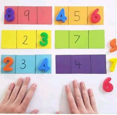 two hands are next to colorful numbers on a white surface and one hand is reaching for the number