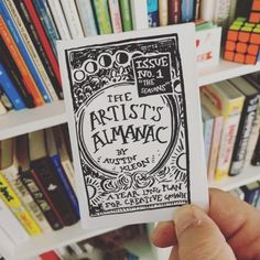 a hand holding up a piece of paper with the words artist's almanac on it