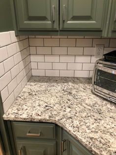 a kitchen counter with green cabinets and white tile on the backsplash is seen in this image