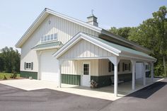 a large white barn with green trim on the roof and side walls, along with an attached parking lot