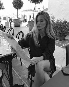 a woman sitting at an outdoor table looking at a piece of paper that she is holding