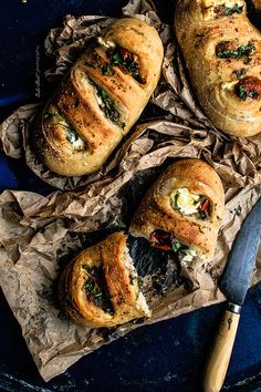 bread rolls with spinach and cheese on top sitting on wax paper next to a knife