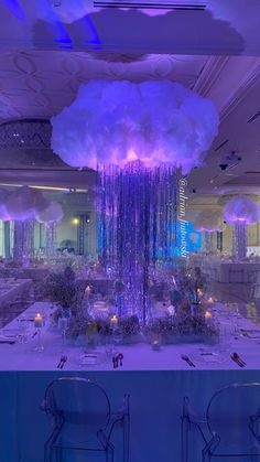 a table is set up for a party with purple lighting and white flowers hanging from the ceiling