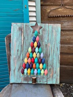 a small christmas tree made out of colored balls on top of a wooden chair in front of a blue door