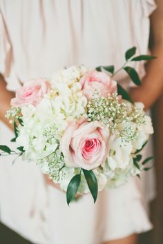 a bridal holding a bouquet of pink roses and white hydrangeas in her hands