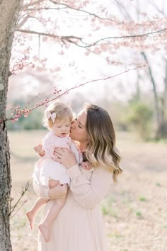 a woman holding a baby in front of a tree with pink blossoms on the branches