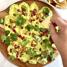 a wooden platter filled with guacamole and pomegranates