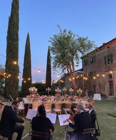 a group of people sitting around a table with musical instruments in front of trees and string lights