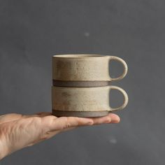 a person holding two coffee cups in their hand on a gray background with space for text