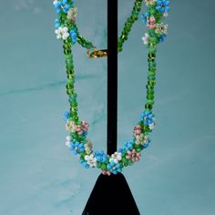 This dainty springtime necklace features three bundles of beaded daisies, woven in a spiral around multicolored green glass beads. The daisies come in shades of pink, blue, white, and cream, each with its own set of tiny leaves. This necklace looks beautiful at a variety of lengths, but was designed to be a choker (14-16in) or princess (18in) necklace. This necklace is made-to-order. Please allow 3-5 business days for processing. Spring Flower Necklace With Round Beads, Turquoise Beaded Jewelry For Spring, Adjustable Green Flower Necklace With Round Beads, Green Round Bead Jewelry For Spring, Green Flower Necklace With Colorful Beads, Handmade Vintage Necklaces For Spring, Spring Green Beaded Jewelry, Green Beaded Jewelry For Spring, Spring Jewelry Making With Tiny Beads