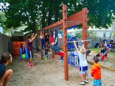 children are playing in the sand at a play area with swings and climbing bars, while adults watch