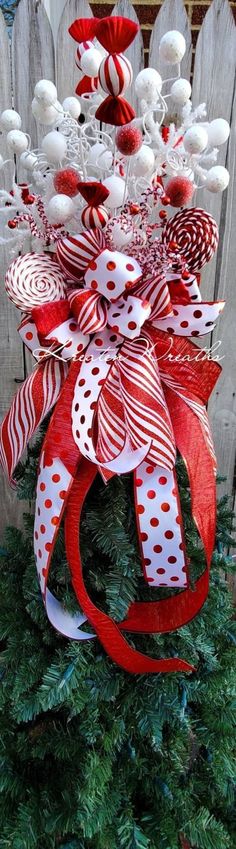 a red and white bow on top of a christmas tree in front of a fence