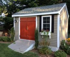 a small shed with a red door and flower boxes on the front window sill