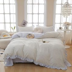 a bed with white comforters and pillows in a room next to two large windows