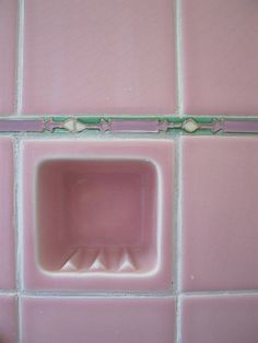 a pink tiled wall with a square hole in the middle and an odd design on it