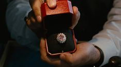 a person holding an engagement ring in a red box