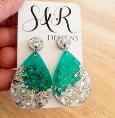 a pair of green and white earrings with glitter on them sitting on top of a wooden table