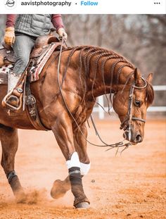 a woman riding on the back of a brown horse across a dirt field with trees in the background