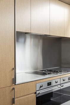 an empty kitchen with stainless steel appliances and wood cabinetry on the walls, along with black flooring