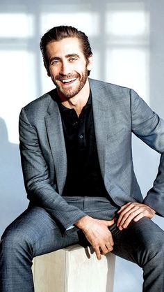 a man sitting on top of a wooden block wearing a suit and smiling at the camera