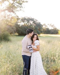 a man and woman standing in tall grass holding an award for their wedding photo shoot