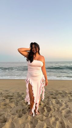 a woman standing on top of a sandy beach next to the ocean wearing a white dress