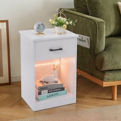 a white night stand with books and a clock on it next to a green chair