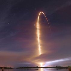 a long exposure shot of a rocket launching into the night sky over a body of water