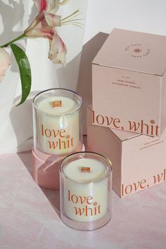 two candles sitting next to each other in front of a pink box with love and whit written on it