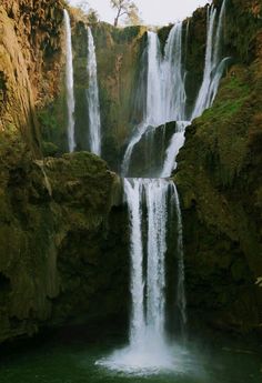 there is a large waterfall in the middle of this body of water that has green moss growing on it