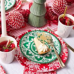 a red and green plate topped with a slice of cake next to two cups of tea