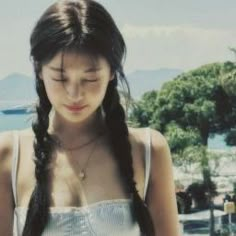 a woman with long hair looking down at her cell phone while standing in front of the ocean