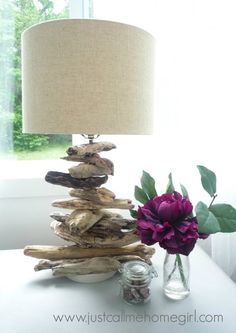 a table with a lamp and some driftwood on it next to a vase filled with flowers