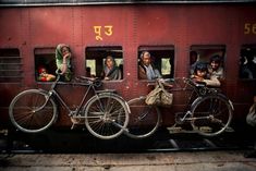 several people are looking out the window of a train car with bicycles parked on it