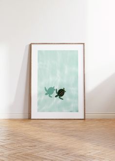 a framed photograph of a turtle swimming in the water on a wooden floor next to a white wall