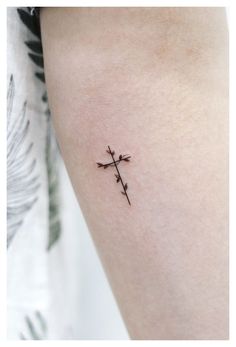 a small cross tattoo on the right arm and leg, with leaves in the background