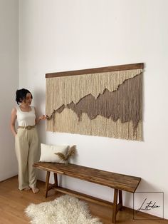 a woman standing next to a wooden bench in front of a wall hanging on the wall