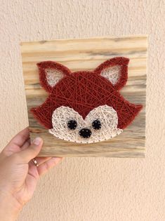 a hand holding up a piece of string art with a red fox face on it