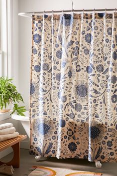 a blue and white floral shower curtain next to a bathtub with a plant in the corner