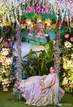 a woman in a purple dress sitting on a swing surrounded by flowers and greenery