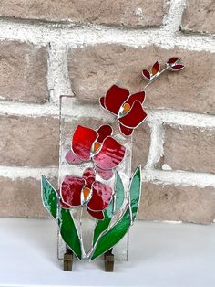 a glass vase with red flowers in it sitting on a table next to a brick wall