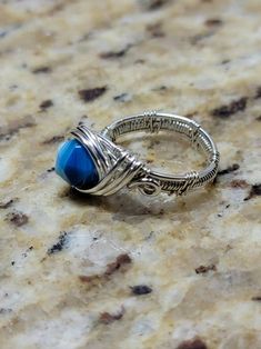 a silver ring with a blue stone on it sitting on a marble counter top,