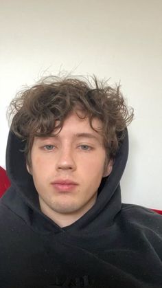 a young man with curly hair wearing a black hoodie and looking at the camera