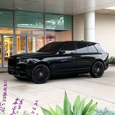 a black suv parked in front of a building with purple flowers on the side walk