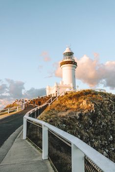 a white lighthouse sitting on top of a hill next to a road and fenced in area