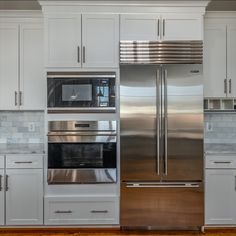 a stainless steel refrigerator and oven in a white kitchen with wood floors, cabinets and drawers