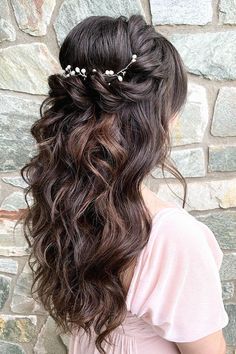 a woman with long dark hair wearing a flowered headpiece in front of a stone wall