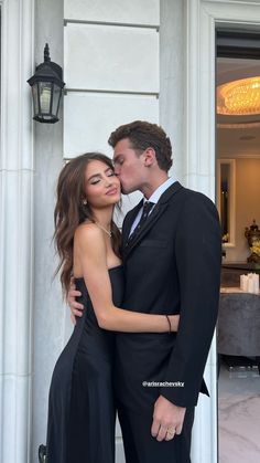 a man in a suit kissing a woman in a black dress on the steps of a building