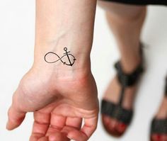 a small tattoo on the wrist of a woman with an anchor and cross in it